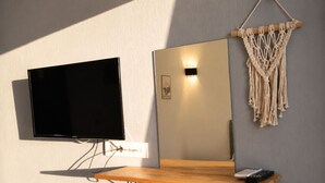 A wall-mounted TV, a mirror, and a macrame wall hanging. - Kent Otel Ayvalık (Ayvalik)