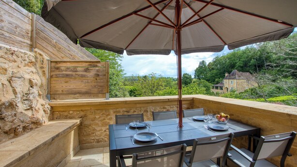 An outdoor patio with a table set for dining, surrounded by stone walls and a large umbrella providing shade.