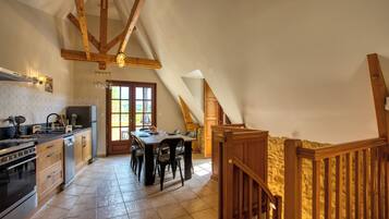 A kitchen with wooden beams, a dining table, and a staircase.