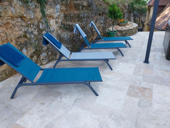 A row of outdoor lounge chairs with metal frames and blue cushions, arranged on a stone patio with a rocky backdrop.