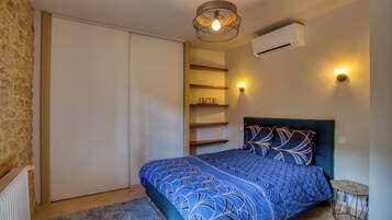 Une chambre à coucher comprenant un lit, un climatiseur fixé au mur, un luminaire au plafond et une petite table avec une chaise.