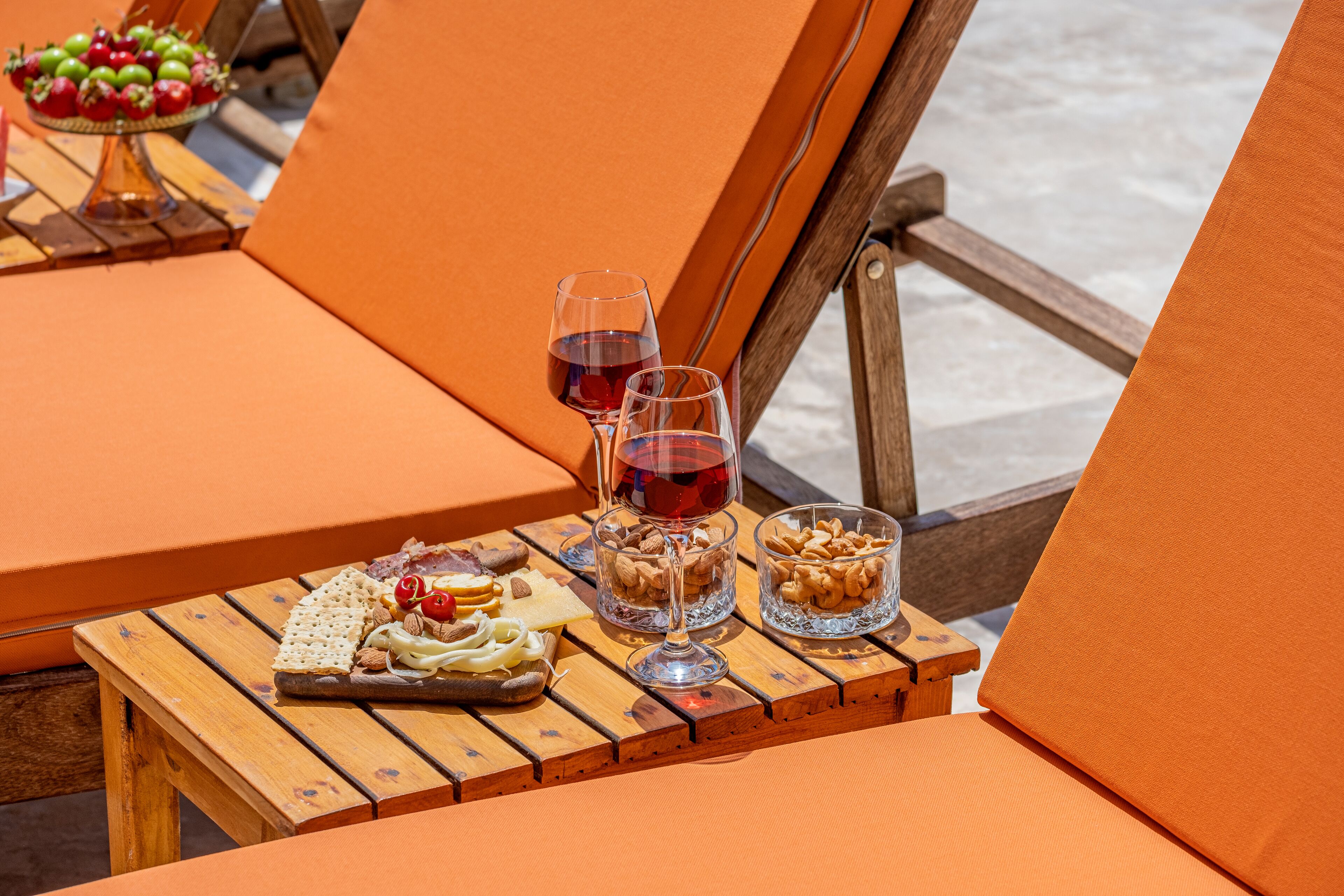 A wooden table with snacks and wine glasses on a sunny outdoor deck.