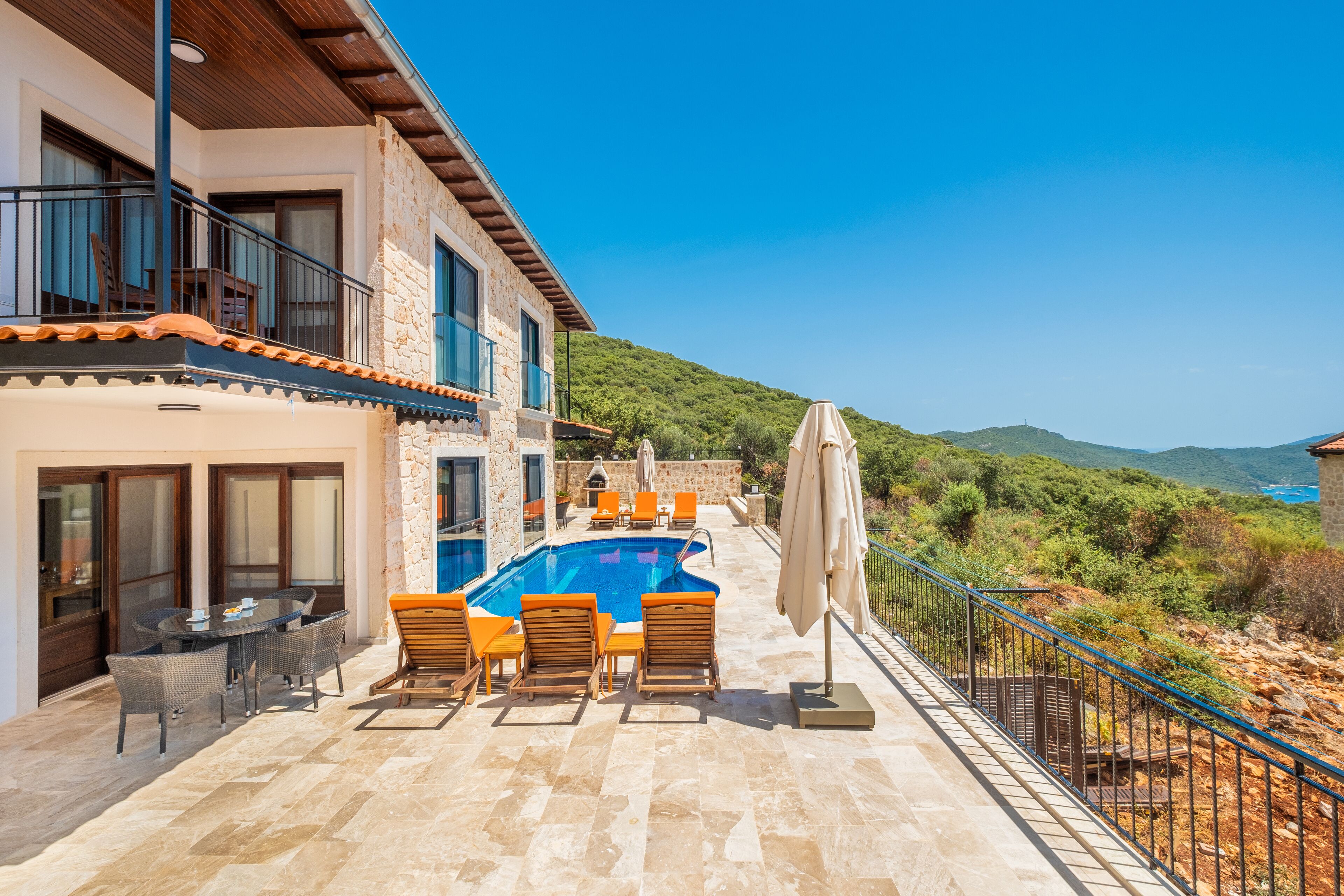 A poolside area with a stone pool, lounge chairs, and a view of the surrounding hills.