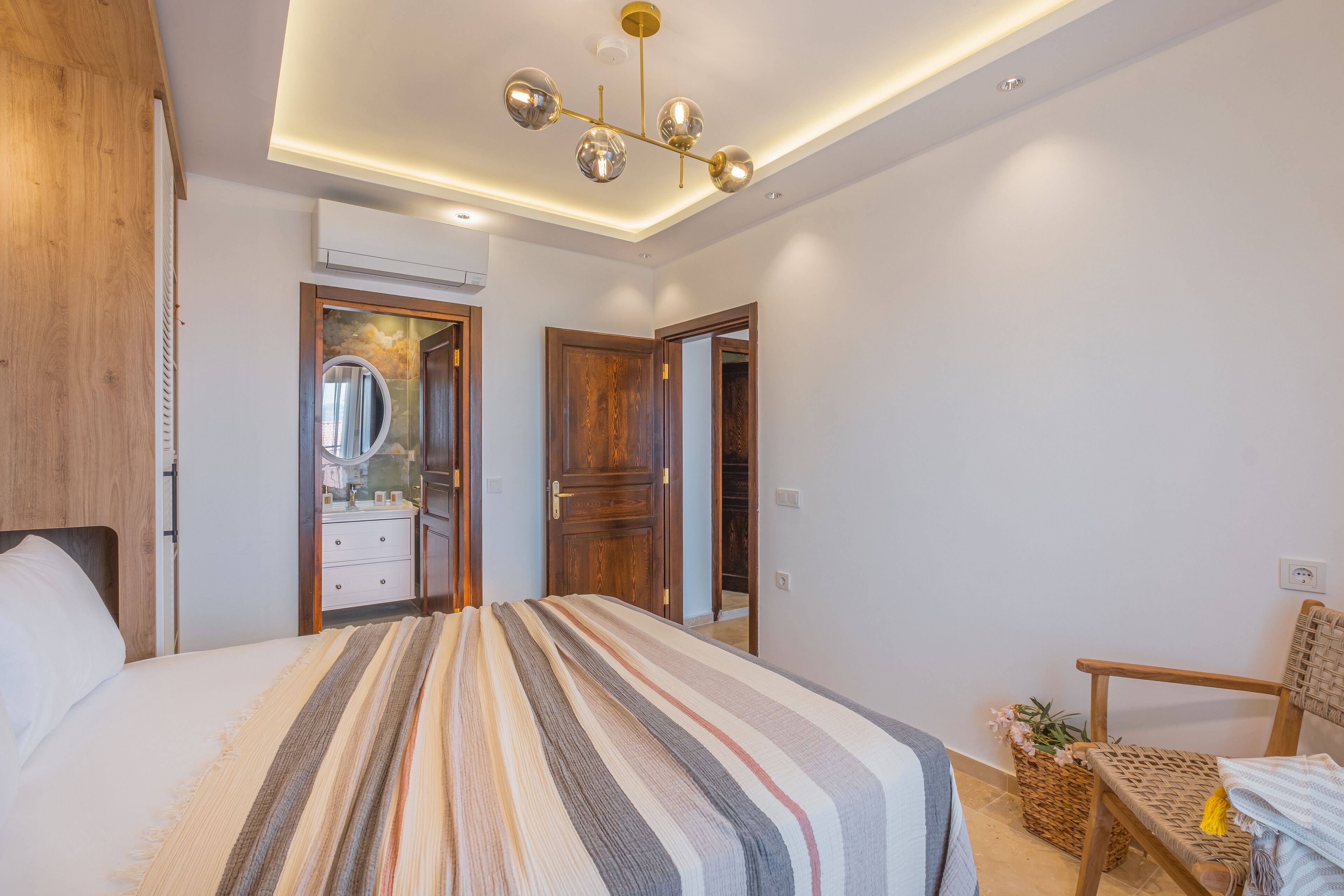 A bedroom with a large bed, a wooden wardrobe, a mirror, and a ceiling light fixture.