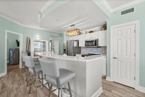 A modern kitchen with a central island, bar stools, stainless steel appliances, and a light teal wall color.