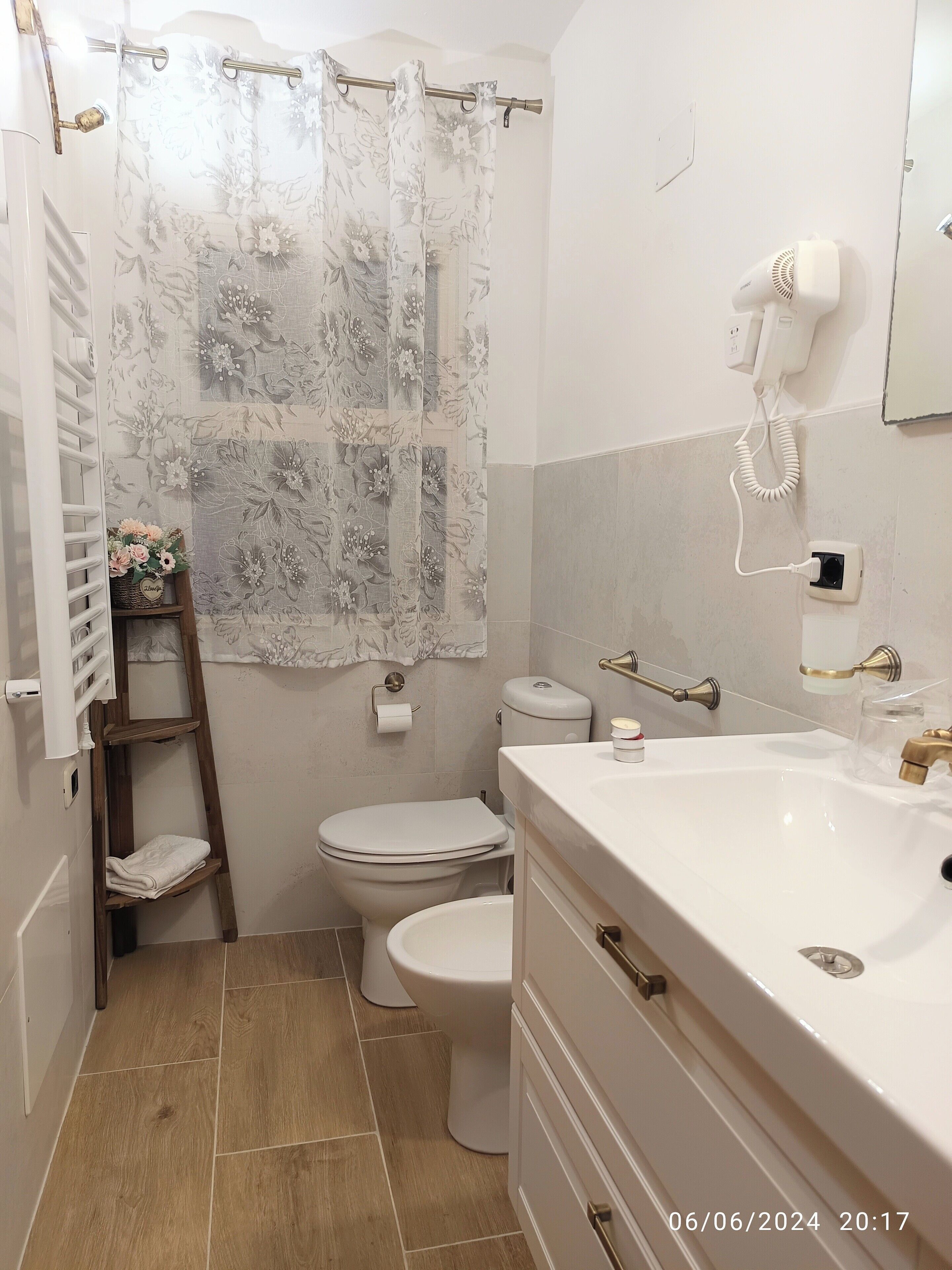Un baño con inodoro, lavamanos, cortina de ducha, secador de pelo y un estante con toallas.
