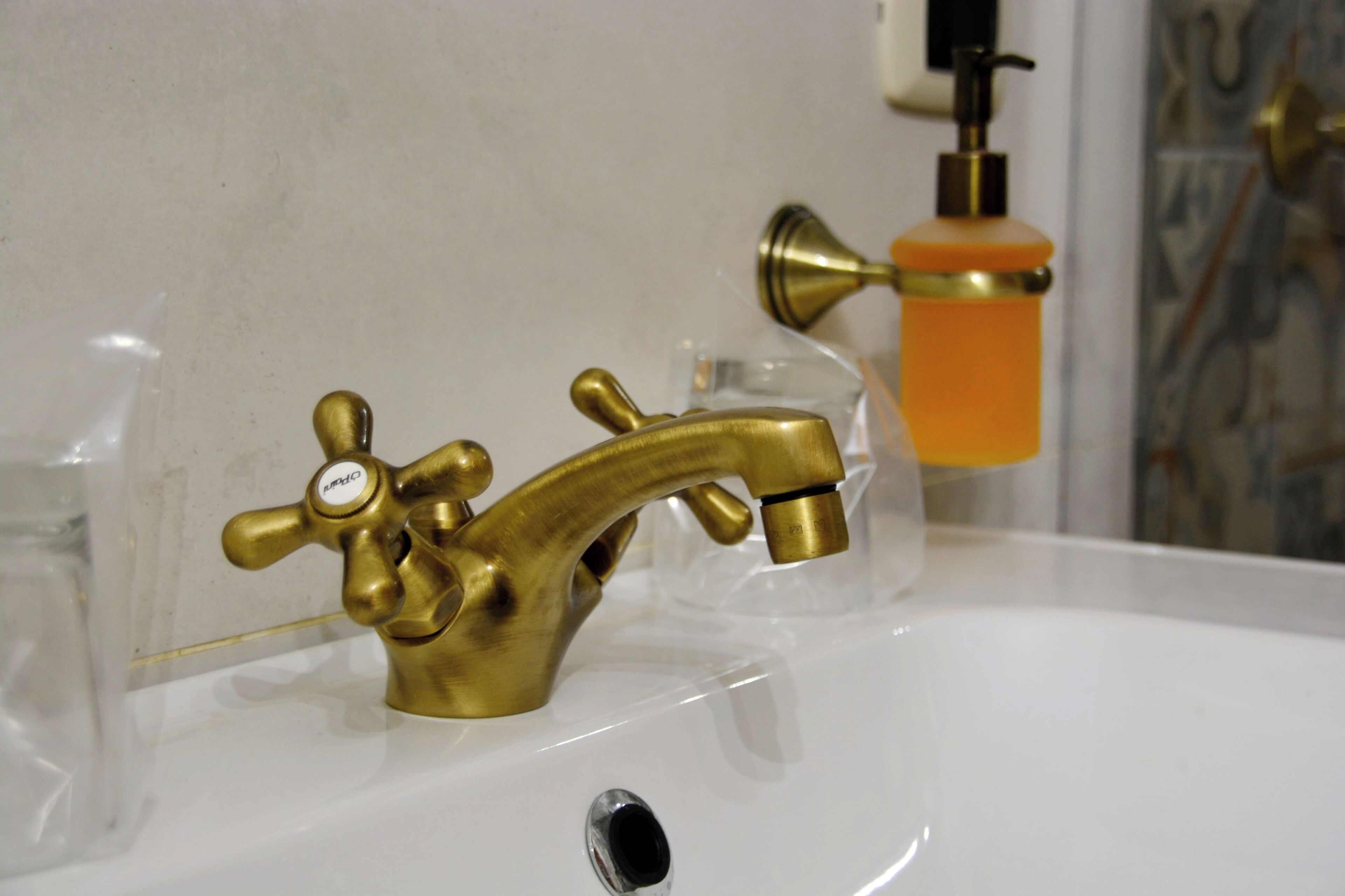 A bathroom sink with a brass faucet and a soap dispenser.