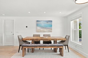 A dining area with a wooden table, cushioned chairs, and a painting of a beach scene.