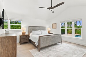 A bedroom with a bed, bedside tables, a ceiling fan, and large windows with a view of greenery.
