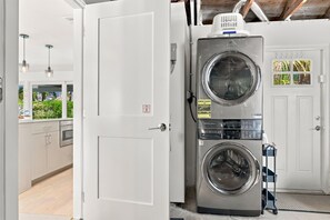 A laundry area with two stacked washing machines and a drying machine, a white door, and a view of the outside through a window.
