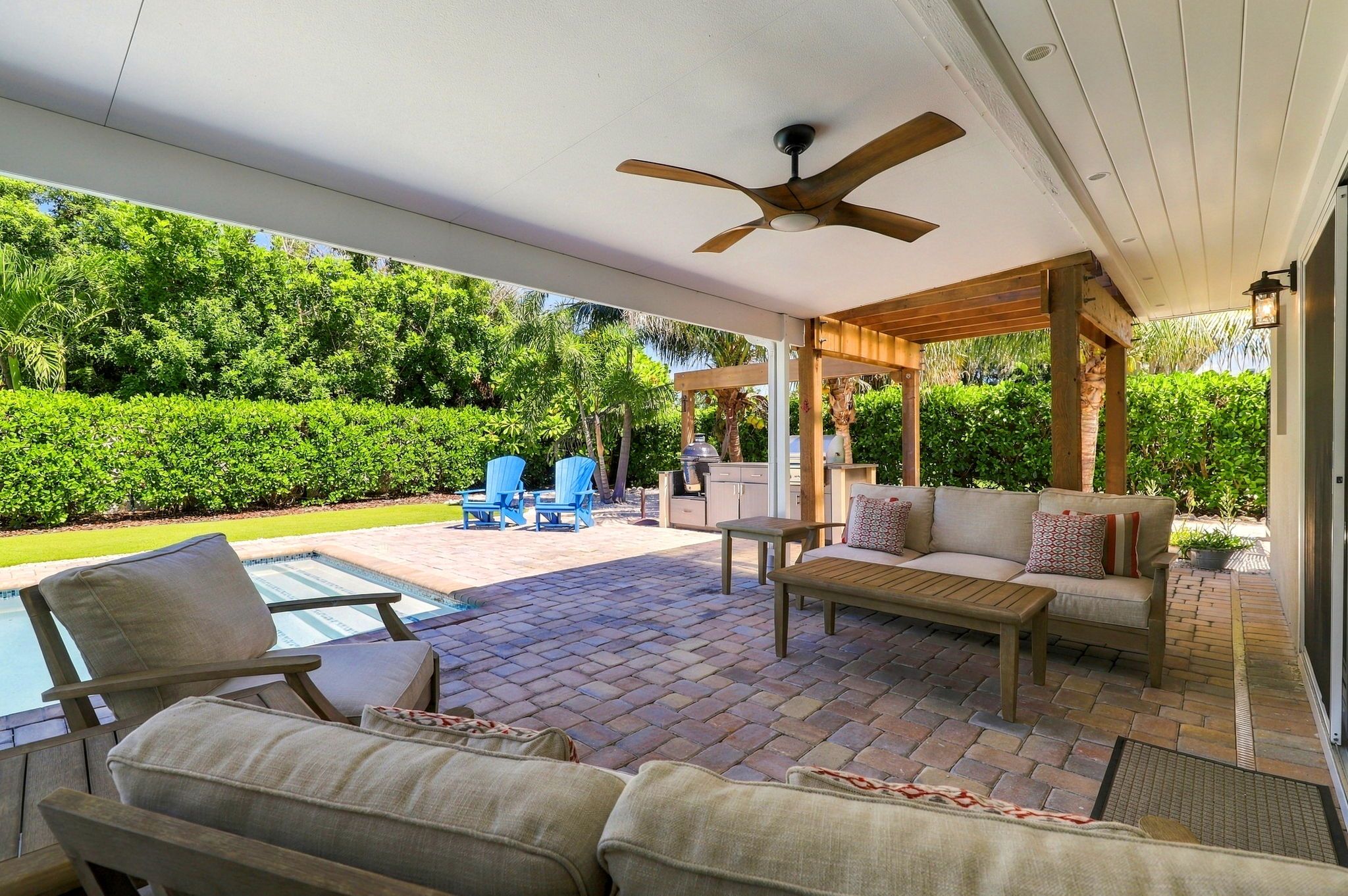 Un patio couvert avec des meubles d’extérieur, un ventilateur de plafond et une vue sur une piscine et un jardin.