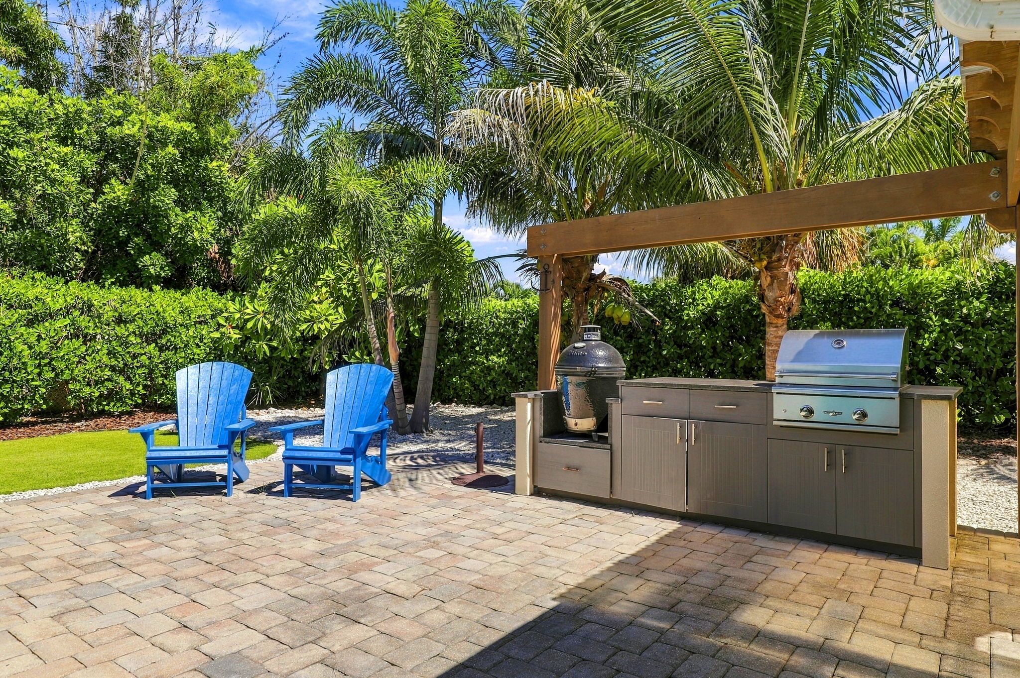 Une terrasse extérieure avec un barbecue, deux chaises Adirondack bleues et une végétation luxuriante en arrière-plan.