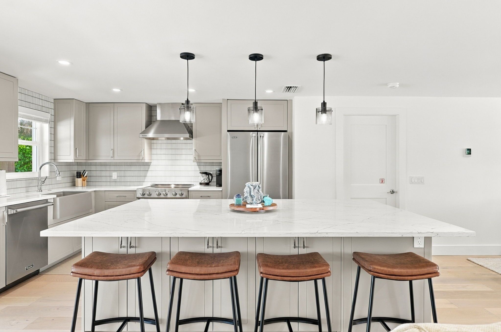 Een moderne keuken met een groot keukeneiland, roestvrijstalen apparatuur en barstoelen.