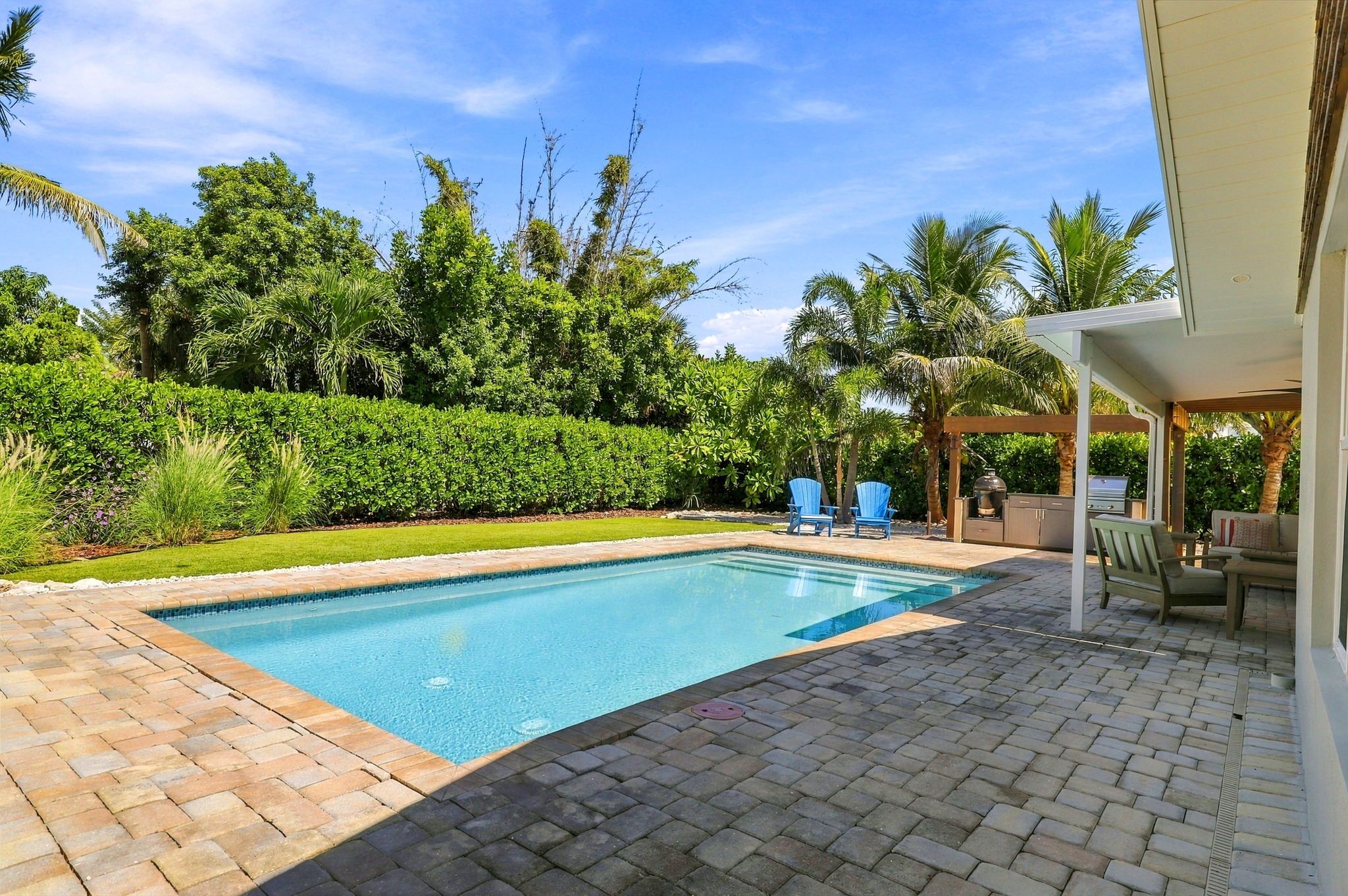A swimming pool with a brick deck, surrounded by lush greenery and palm trees.