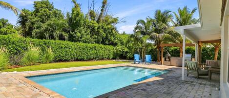A swimming pool with a brick deck, surrounded by lush greenery and palm trees.