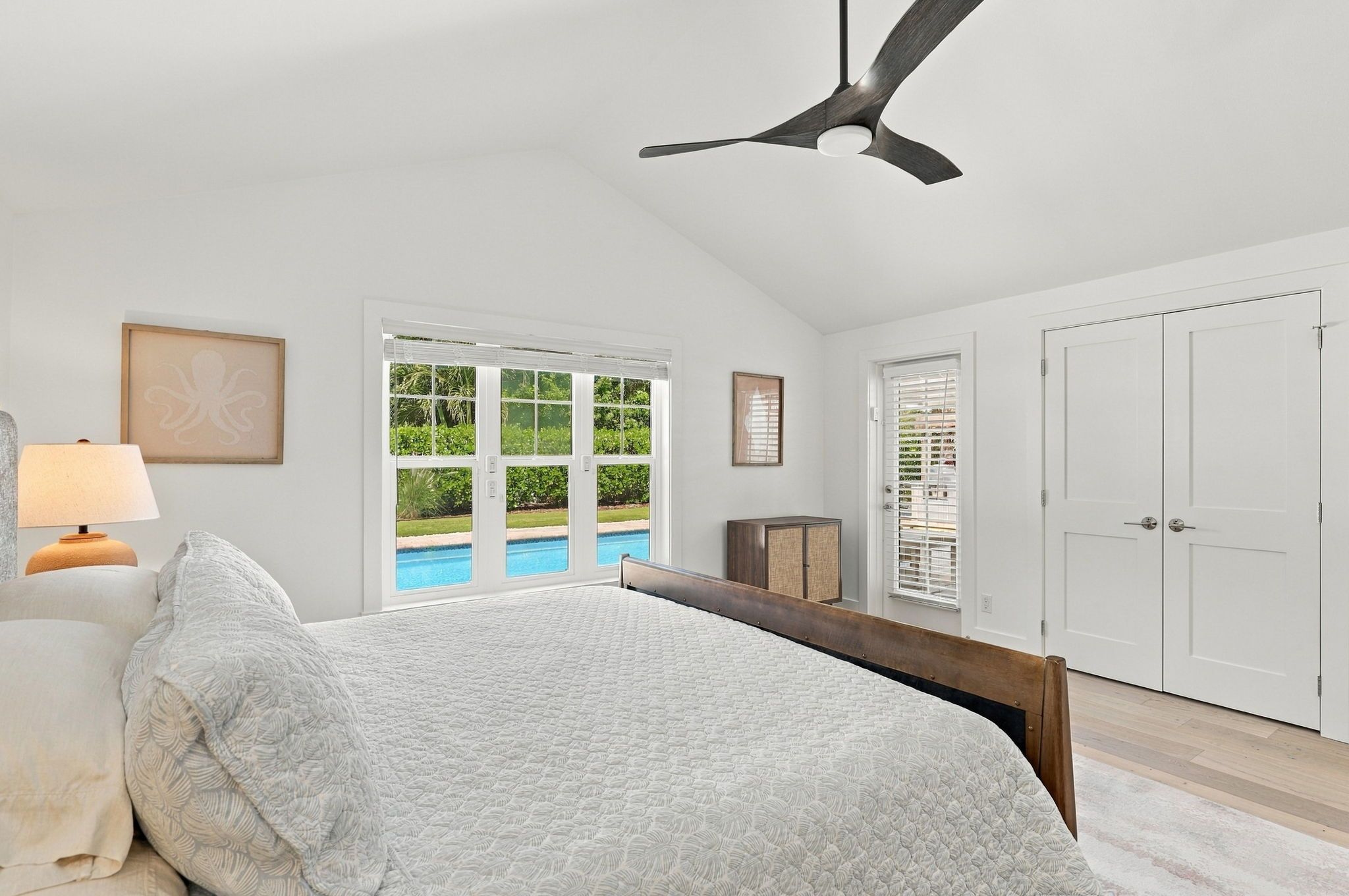 A bedroom with a bed, a ceiling fan, a window with a view of a pool, and a door with a closet.