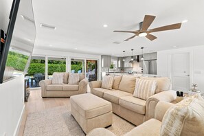 A modern living room with a large sofa, a coffee table, and a ceiling fan. - So Beachy Chic · Renovated 2025 · Private Pool · Two Chef Grills (Holmes Beach)