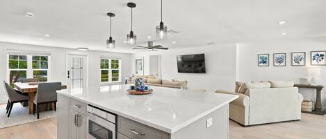 A modern kitchen with a large island, built-in oven, and a dining area with a table and chairs.