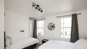 Une chambre d’hôtel avec deux lits simples, une horloge murale ronde et une fenêtre avec des rideaux.