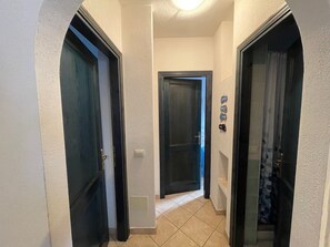 Een smalle gang met drie deuren, waarvan er één openstaat en een badkamer met douchegordijn onthult.