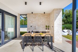 Un espace extérieur aménagé pour les repas, avec un mur en briques, une table en bois et des chaises noires.