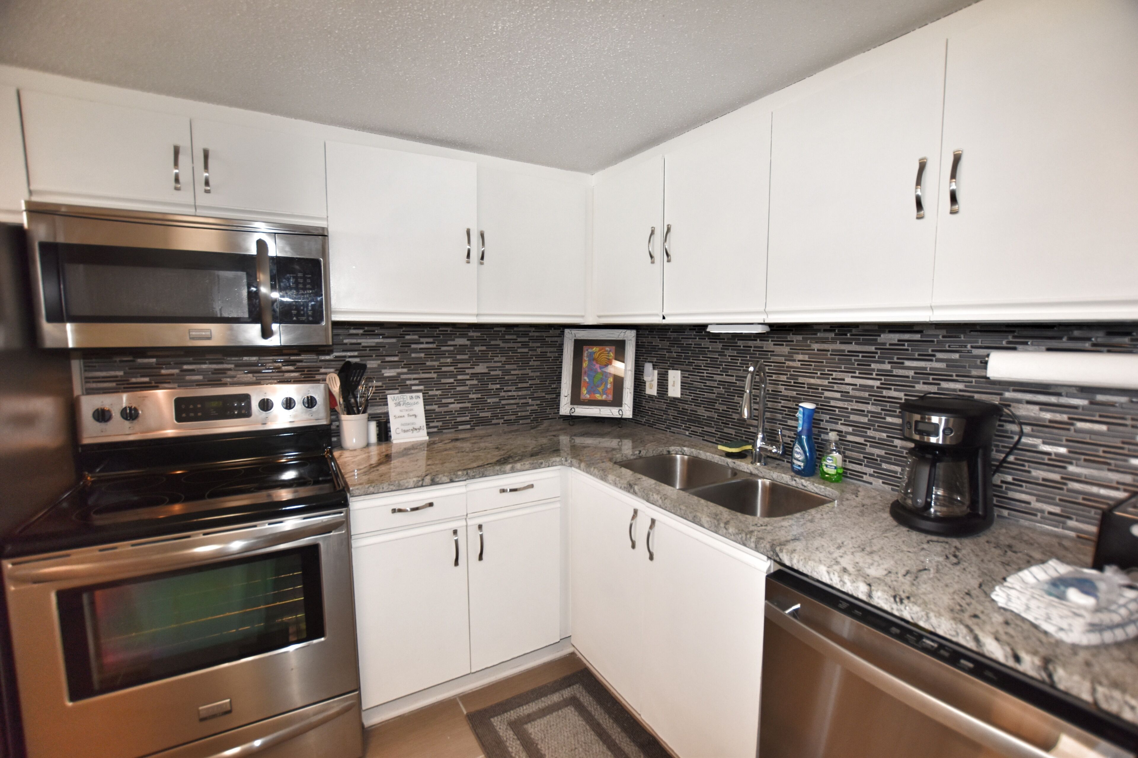 A modern kitchen with stainless steel appliances, white cabinets, a granite countertop, and a backsplash with black tiles.