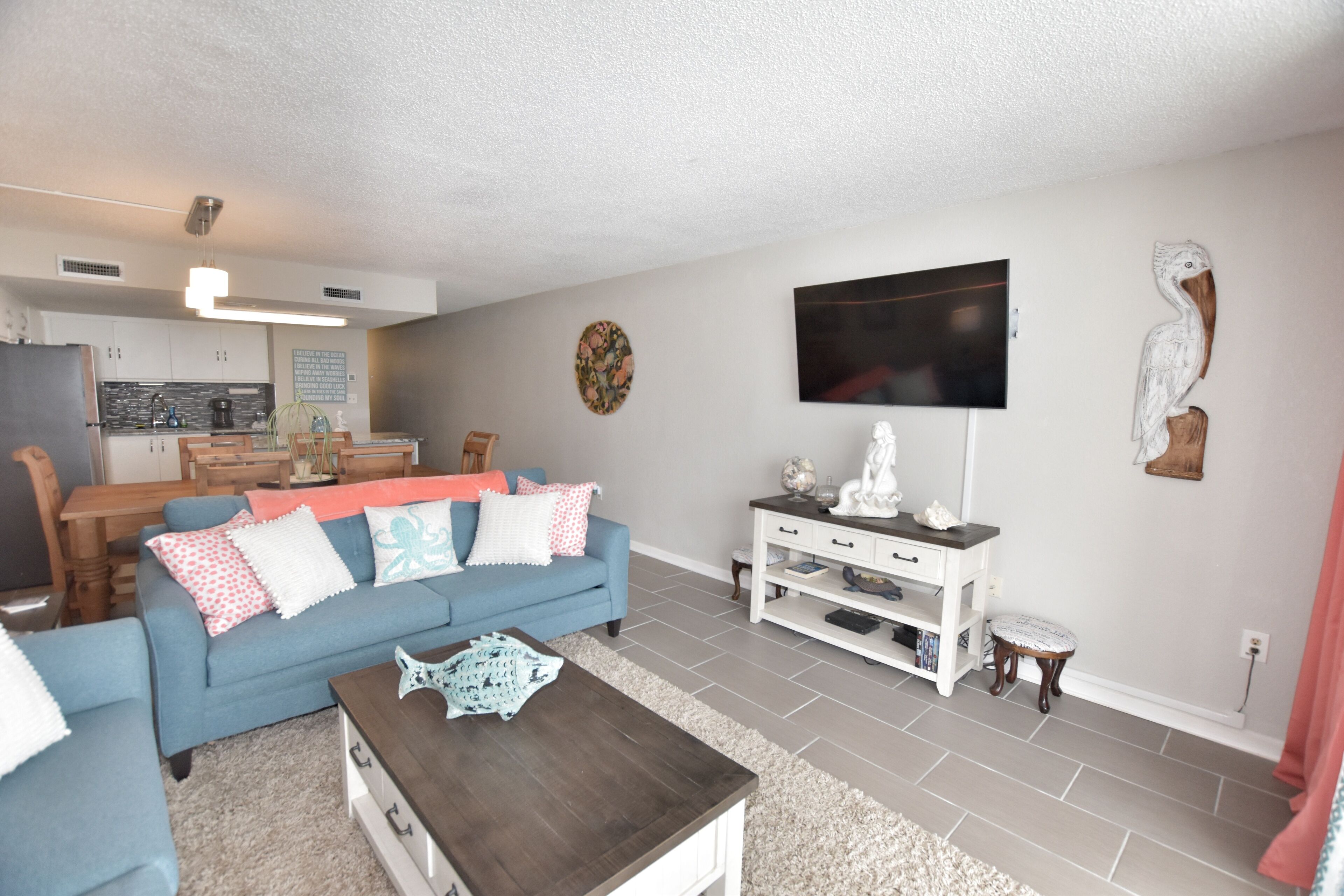 A living room with a blue sofa, coffee table, and a flat-screen TV mounted on the wall.