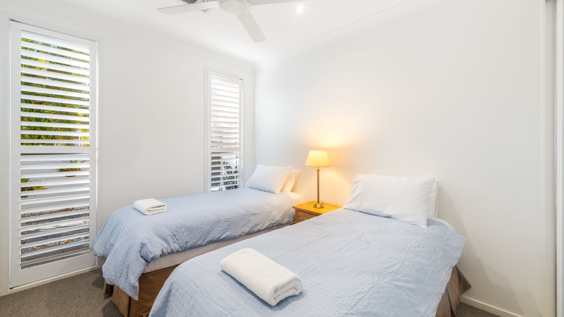 A bedroom with two beds, a nightstand with a lamp, and a ceiling fan.