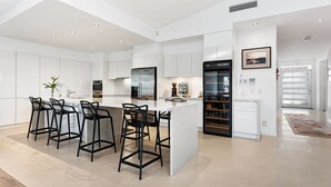 A modern kitchen with white cabinetry, a central island with bar stools, stainless steel appliances, and a glass-enclosed refrigerator.