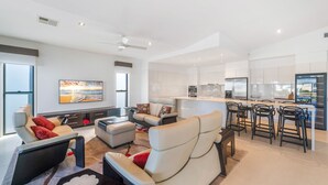 A spacious living area with a sofa, ottoman, and a coffee table. There is a kitchen area with a refrigerator, stove, and bar stools.