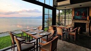 A restaurant with large windows overlooking a body of water and mountains, featuring wooden tables and chairs. - Hotel Labiatan (Shkodër)