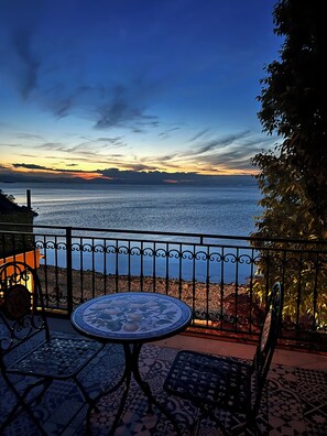 A terrace with a table and chairs, overlooking a body of water and distant mountains.