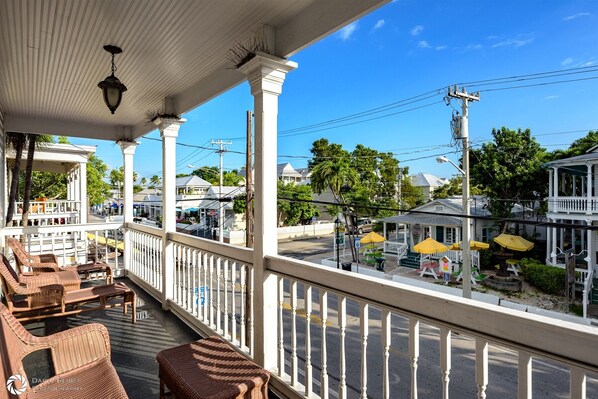 A covered porch with wicker furniture, a view of the street, and a clear blue sky.