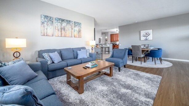 A modern living room with a sofa set, a wooden coffee table, and a dining area with blue chairs. - Vista Cay Luxury Rhapsody 3 Bedroom Condo by RedAwning (Orlando)