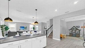 Une cuisine moderne avec des meubles blancs, un plan de travail gris et des luminaires suspendus.