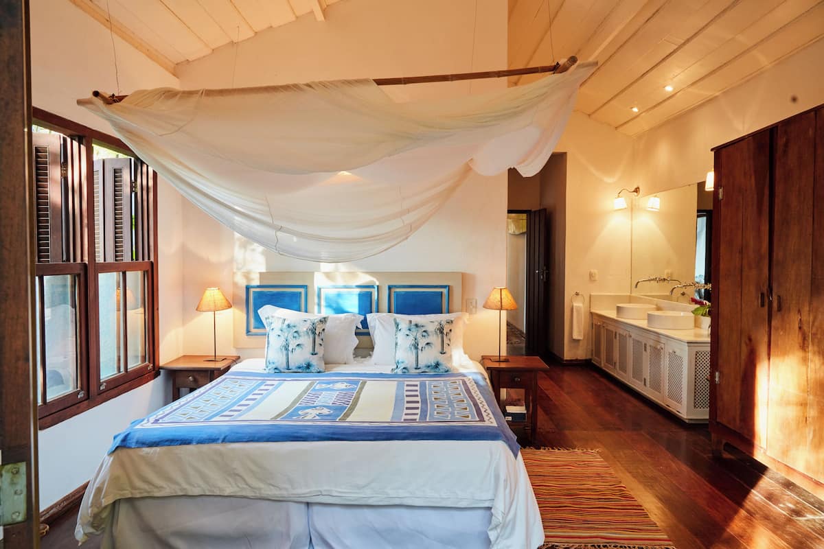 Ein Schlafzimmer mit einem großen Bett, einem Baldachin, einem Nachttisch, einer Lampe, einem Badezimmer mit Waschbecken und Spiegel sowie Holzböden.