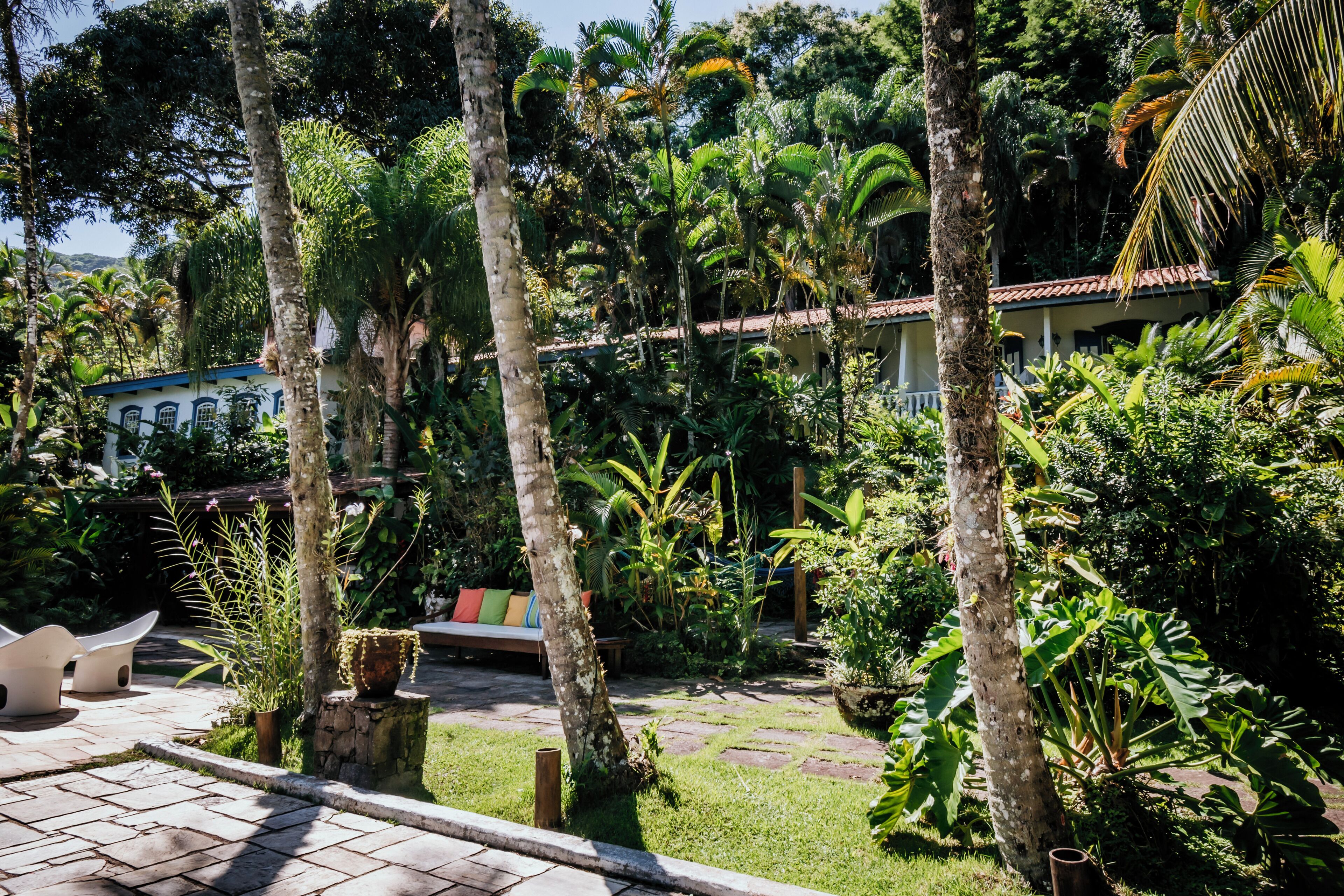 A lush garden with palm trees, a stone pathway, and a building with a red roof.
