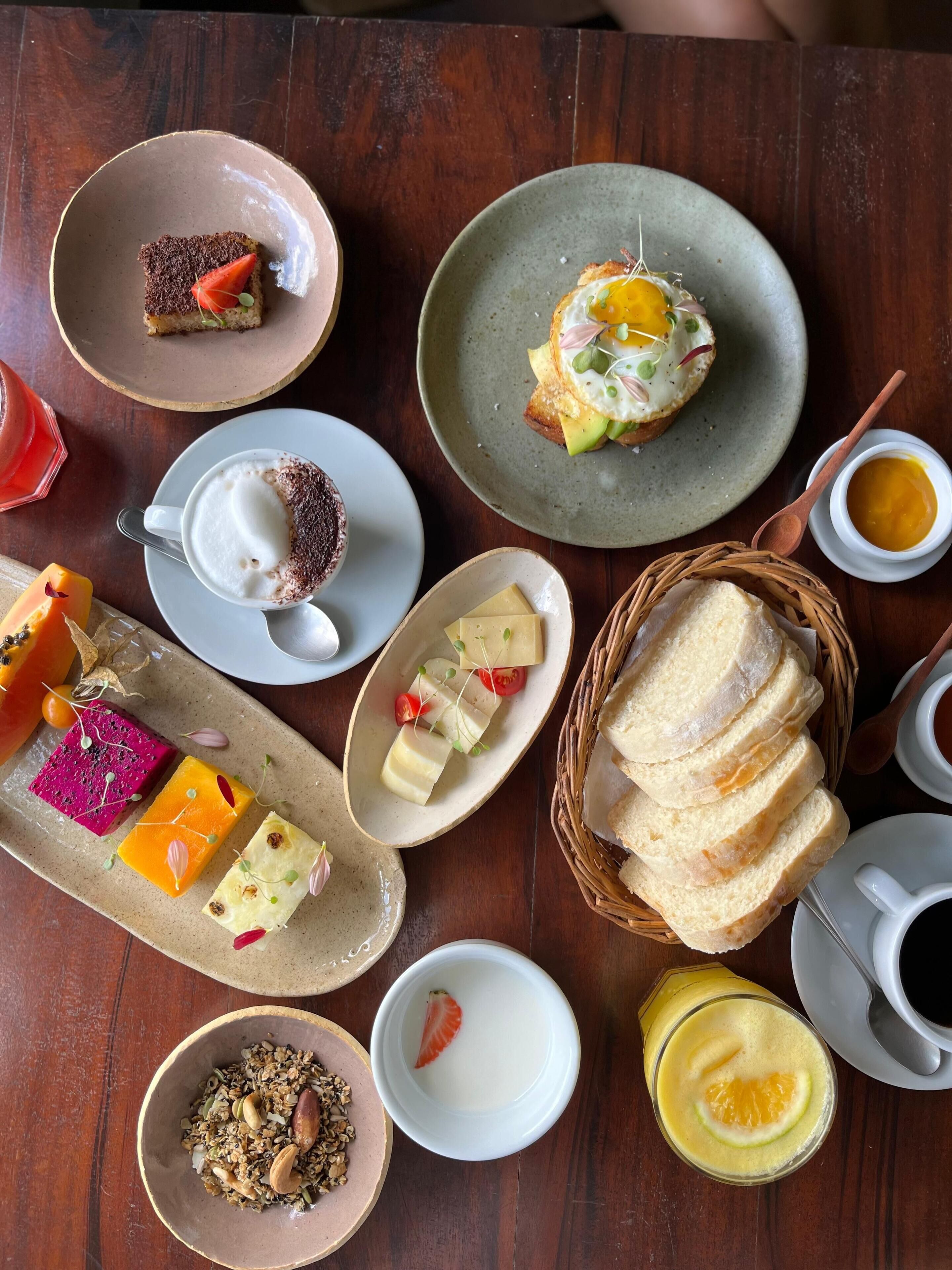 Une variété d’aliments pour le petit-déjeuner, notamment des toasts, des œufs et des fruits, disposés sur une table en bois.