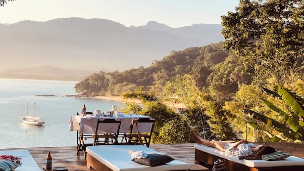 Ein Poolbereich mit Liegestühlen und einem Esstisch, mit Blick auf Strand und Berge.