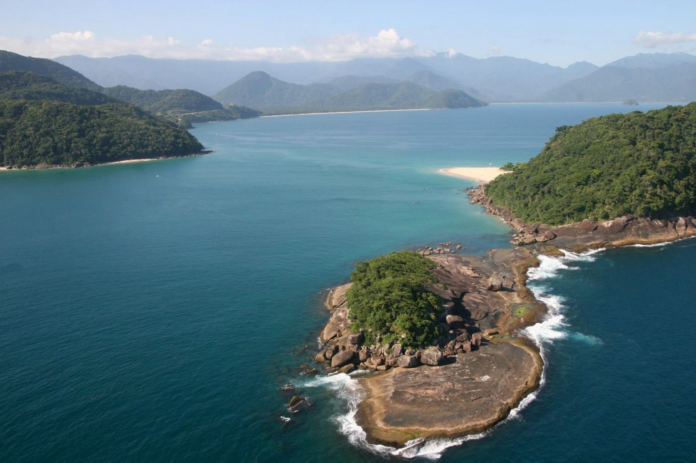 A coastal landscape with a large body of water, a sandy beach, and lush green hills.