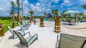 Un espace aménagé au bord de la piscine, avec des chaises longues, des palmiers et un ciel dégagé.