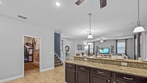 A spacious kitchen with dark brown cabinets, a granite countertop, and a large island. There is a dining area with a television and artwork on the wall.