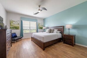 A bedroom with a wooden bed, a nightstand, a dresser, a ceiling fan, and a window with blinds.