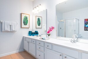 A modern bathroom with a white vanity, a large mirror, and framed leaf artwork.