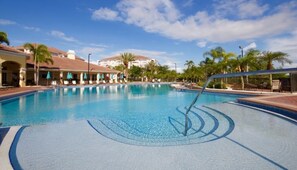 A swimming pool with lounge chairs and umbrellas, surrounded by palm trees and hotel buildings.