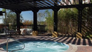 Un área de jacuzzi con una pérgola, rodeada por un patio de ladrillo y una cerca.