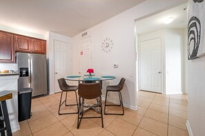 A compact kitchen with a refrigerator, a coffee machine, and a dining table with four chairs.