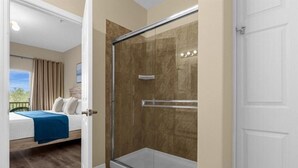 A room with a glass-enclosed shower, a bed with a blue blanket, and a view of the outdoors. - Oakwater Retreat 3 Bedroom Condo (Kissimmee)