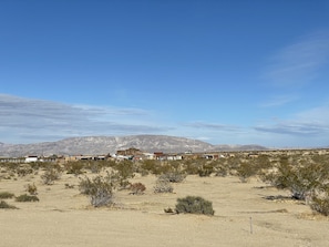 Paisaje desértico con vegetación escasa, algunos edificios y montañas al fondo.