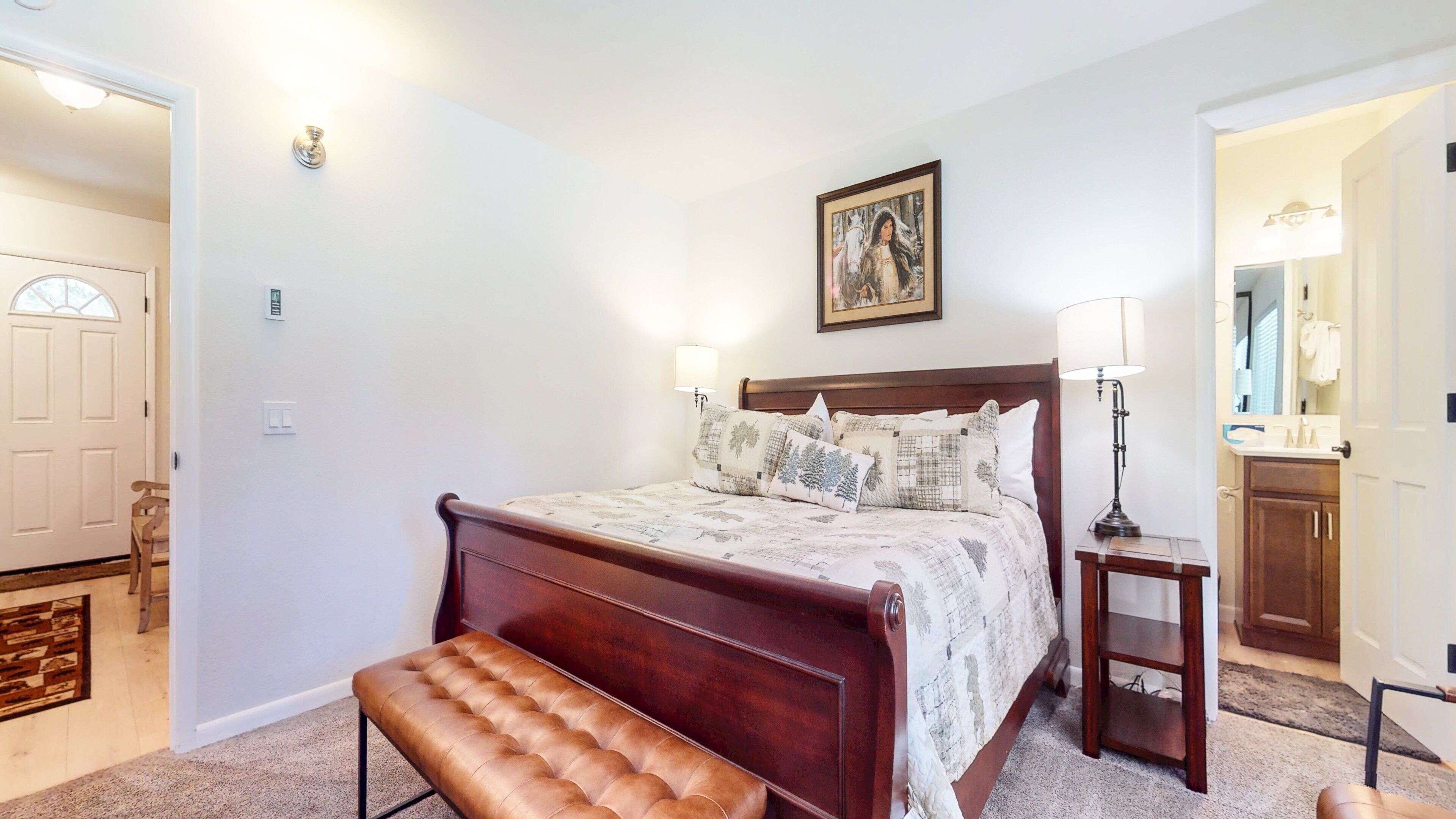 A bedroom with a wooden bed, bedside lamps, a bench, and a painting on the wall.
